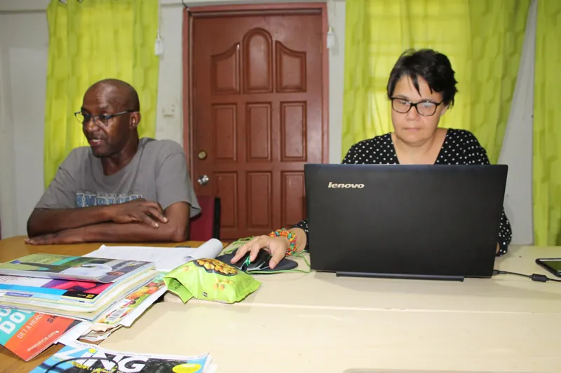 Two people working at a table with a laptop and printed resources